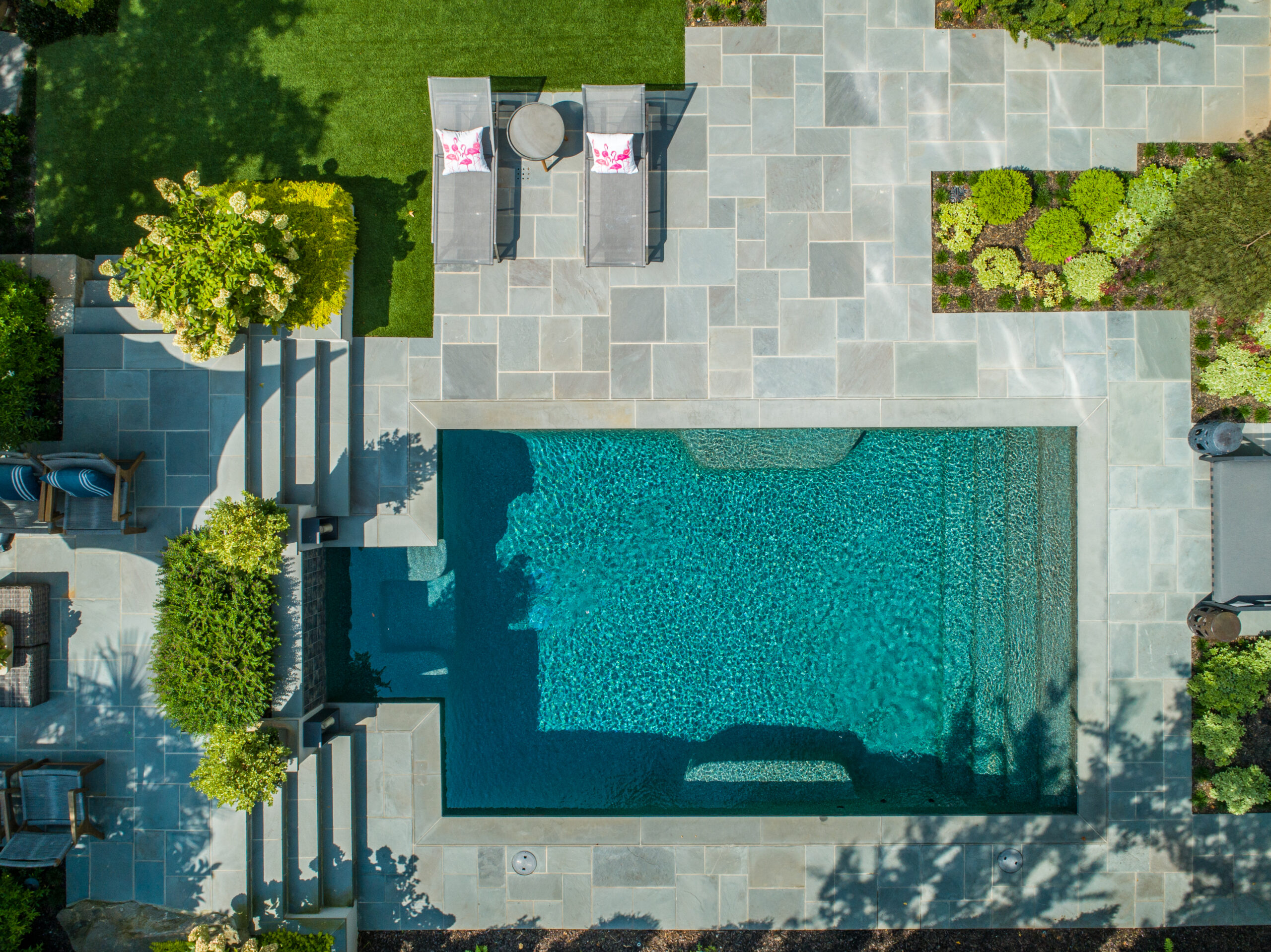 Overhead view of a modern pool with stone terraces and lounge chairs surrounded by greenery