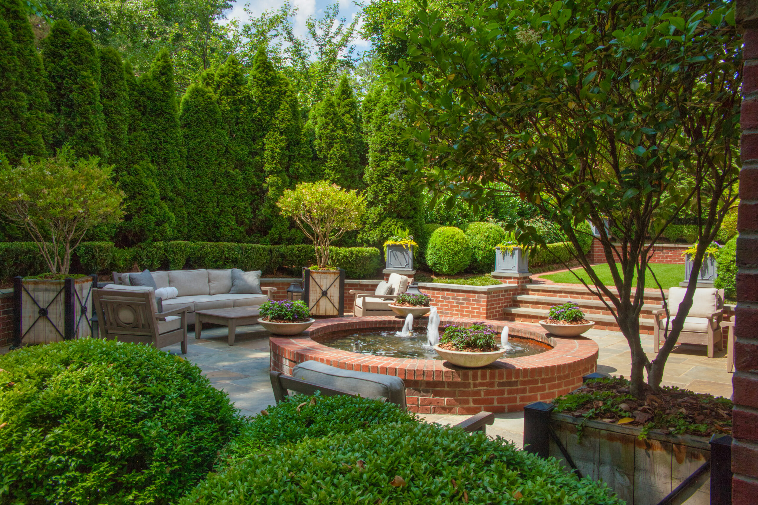 A brick fountain surrounded by greenery with a seating area