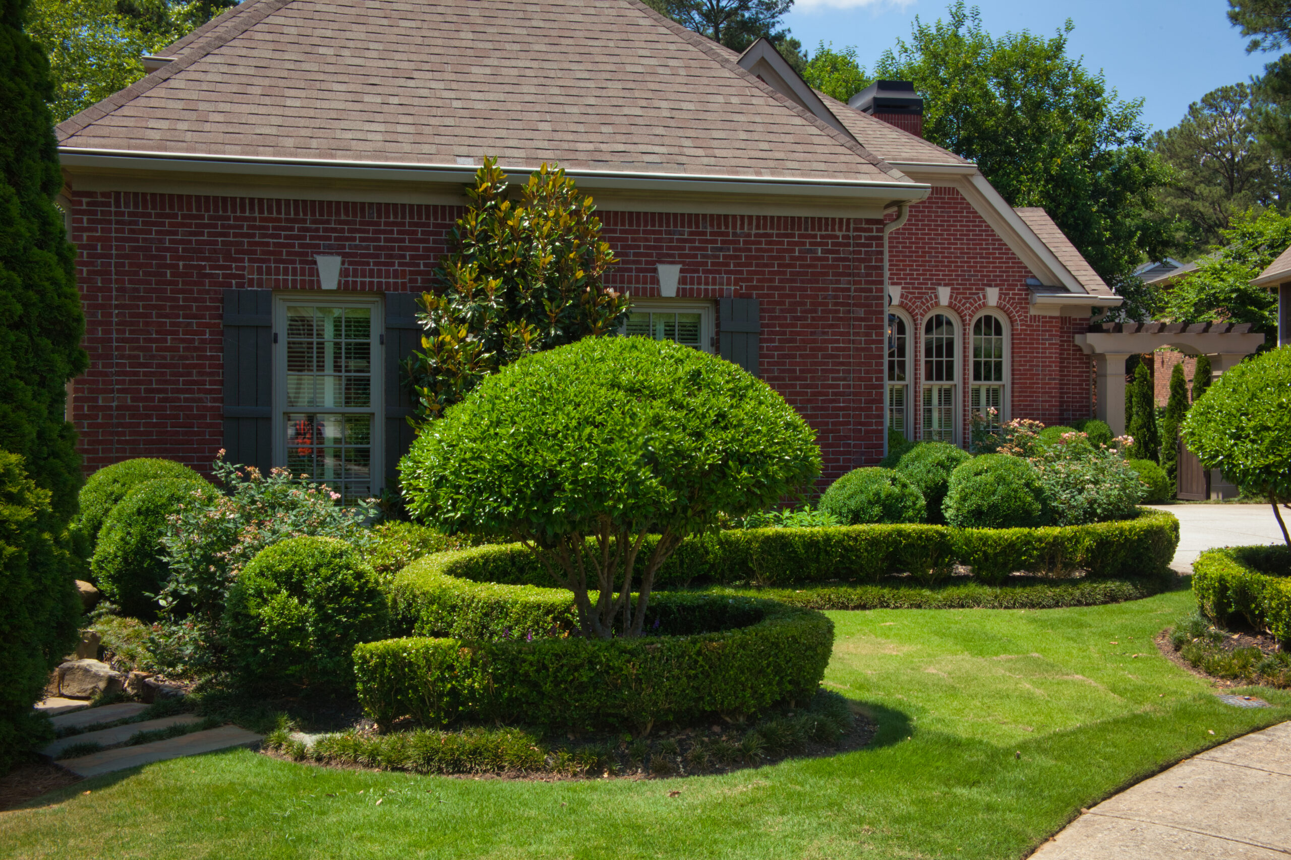 The side view of a brick house with manicured, curving hedges and greenery