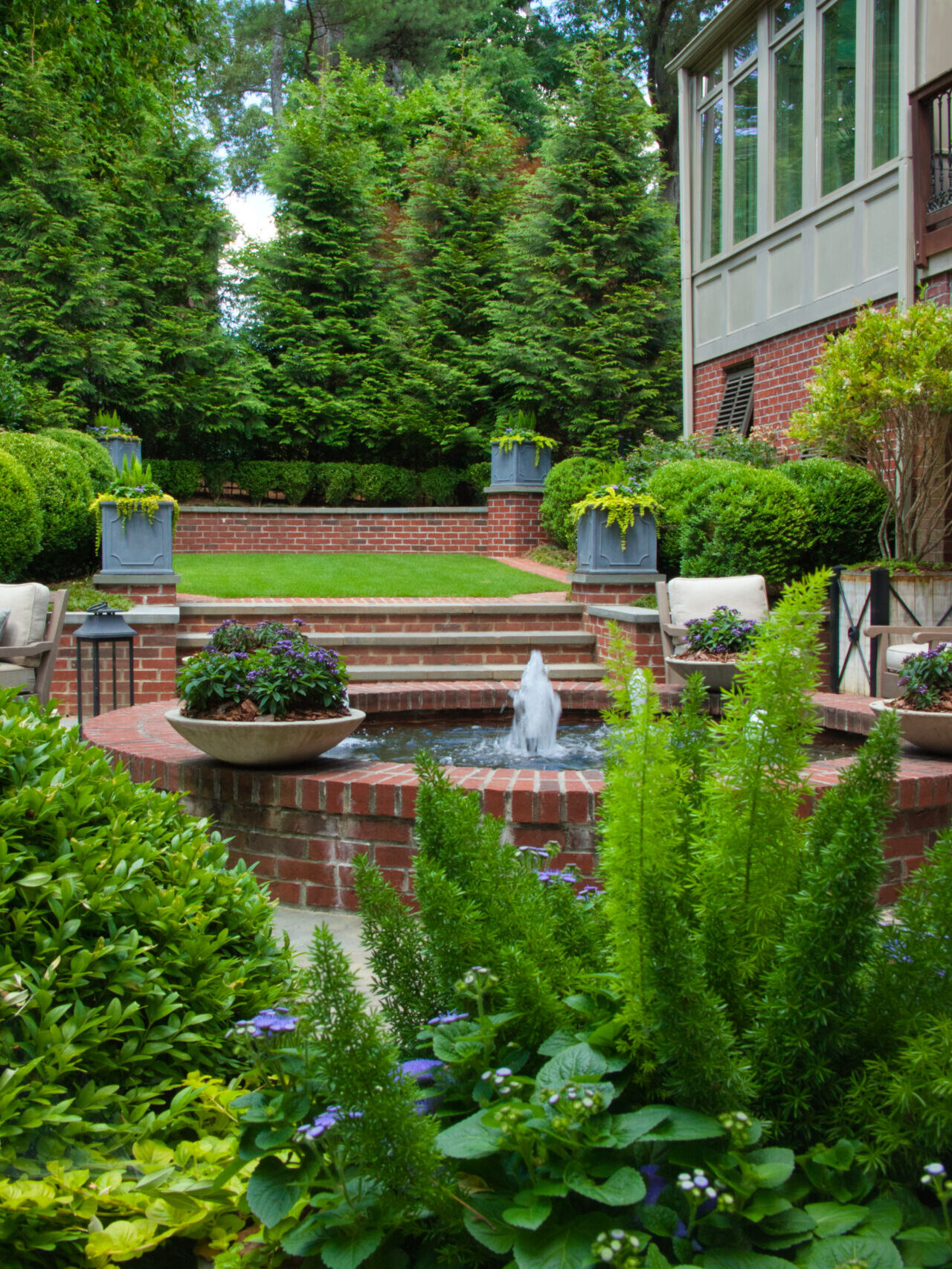 The backyard of a brick house with greenery and a fountain