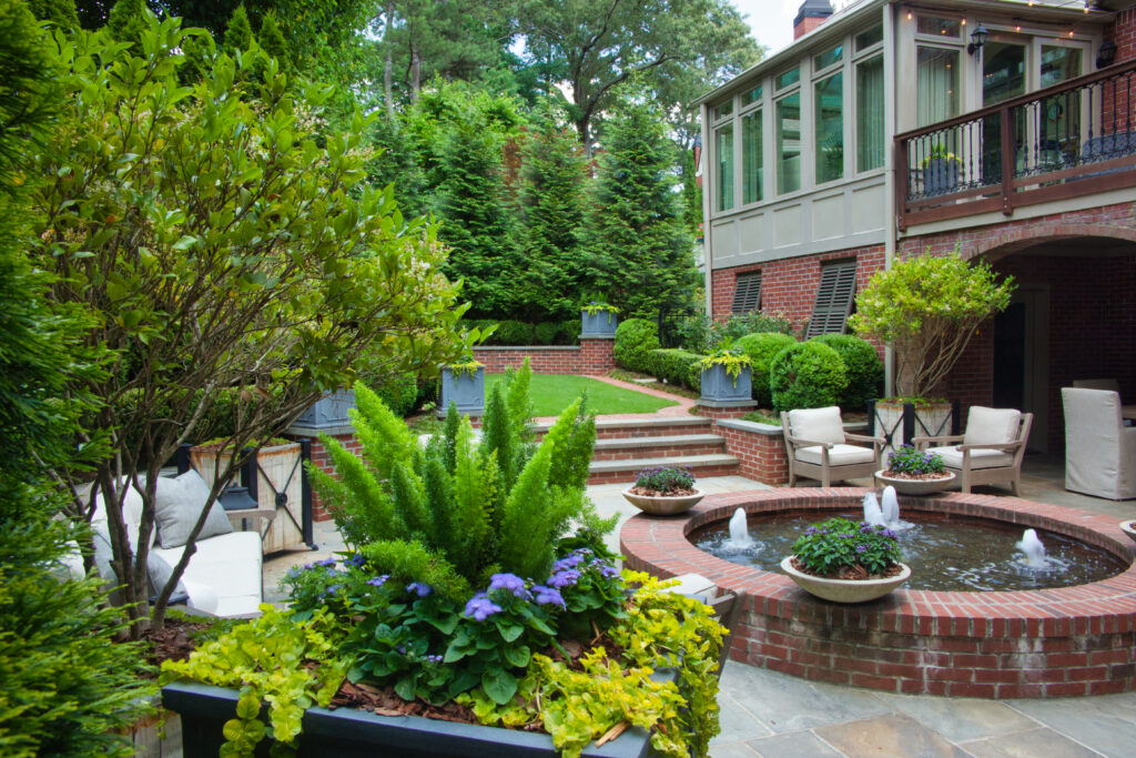 The backyard of a brick house with a fountain, sitting areas and greenery