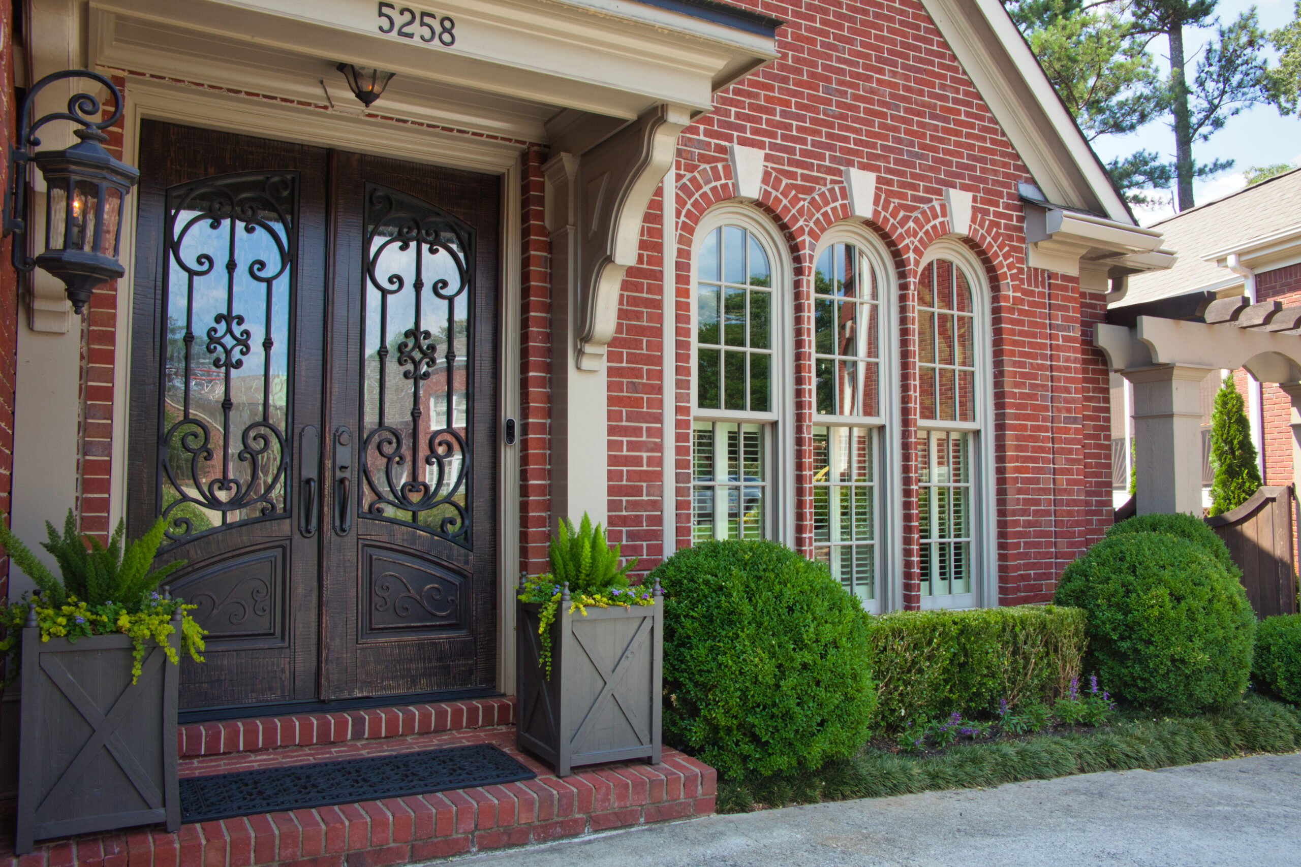 An elegant double door entrance to a brick house with hedges under the windows