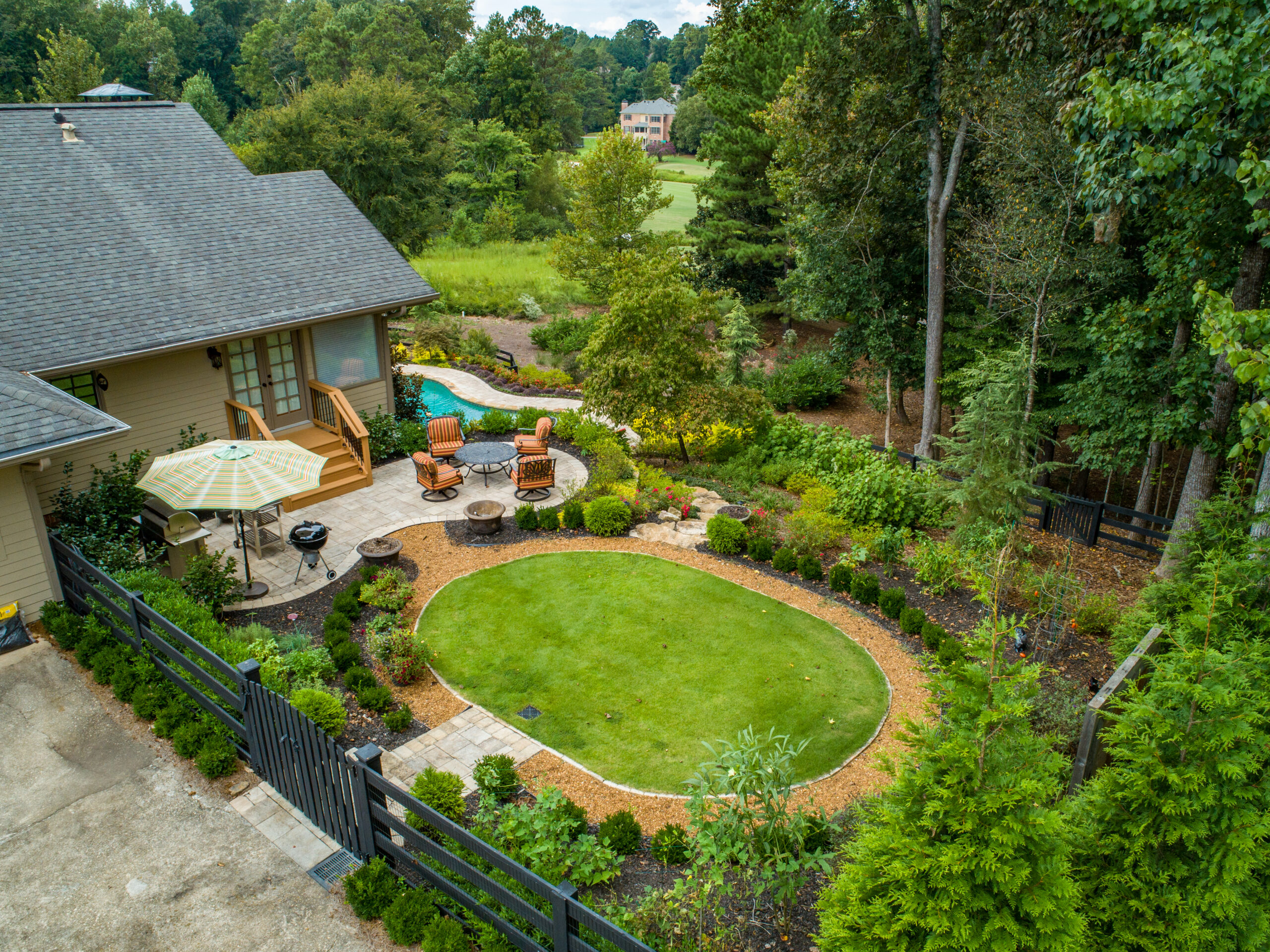 a grass terrace beside a house with a grilling and eating area surrounded by landscaping and greenery