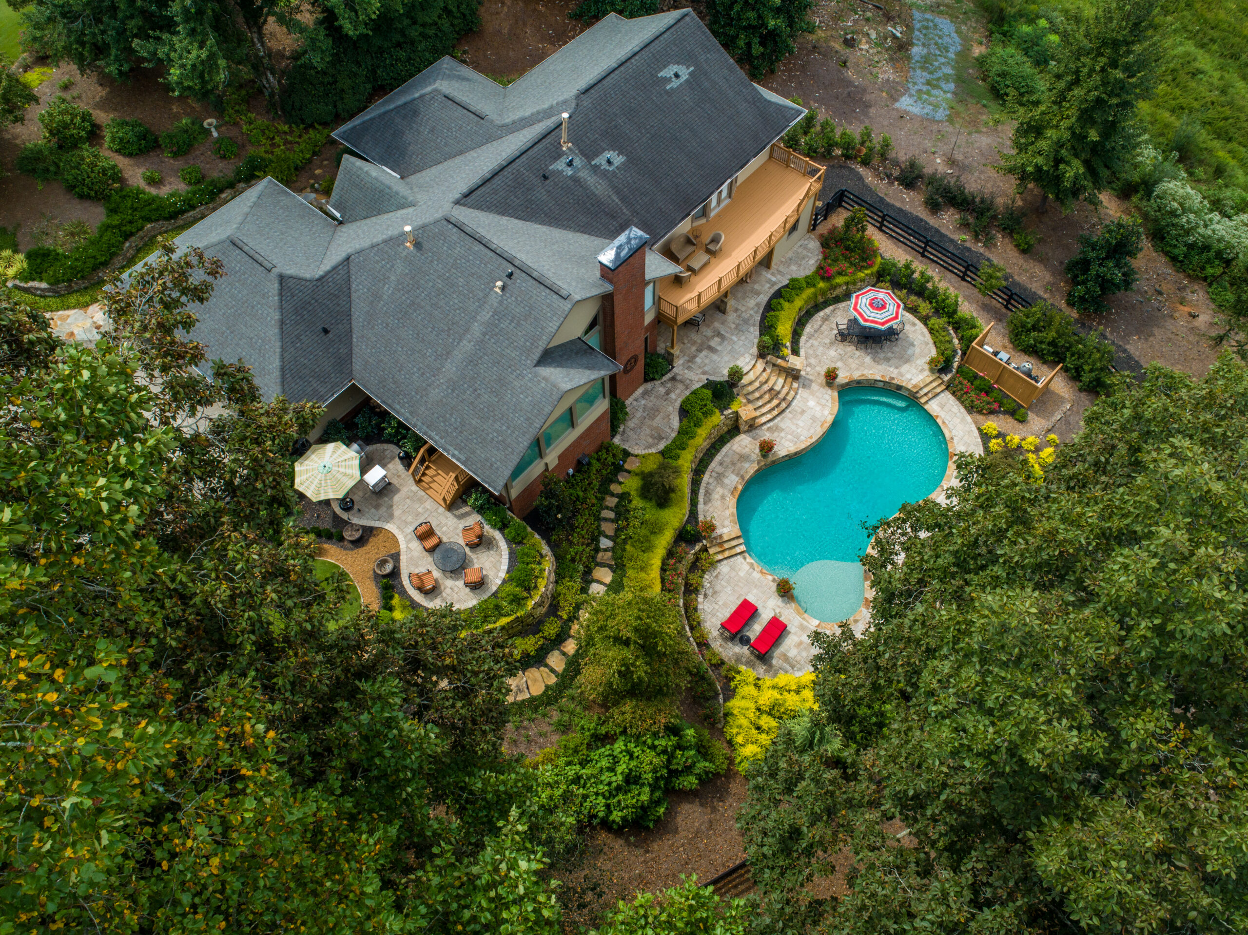 A drone shot above a backyard with a pool surrounded by lush greenery