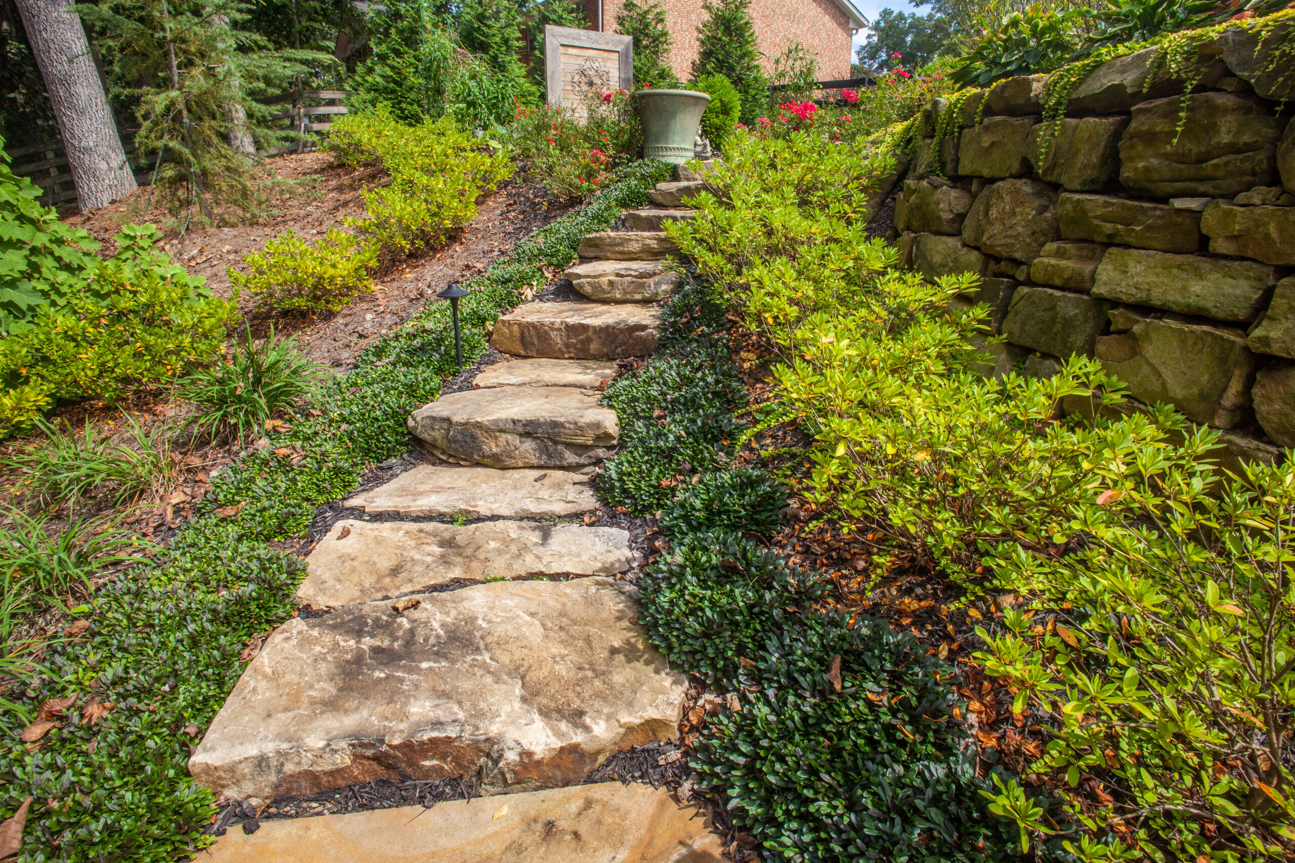 a stepping stone path leading up a small hill surrounded by ornamental grasses and greenery