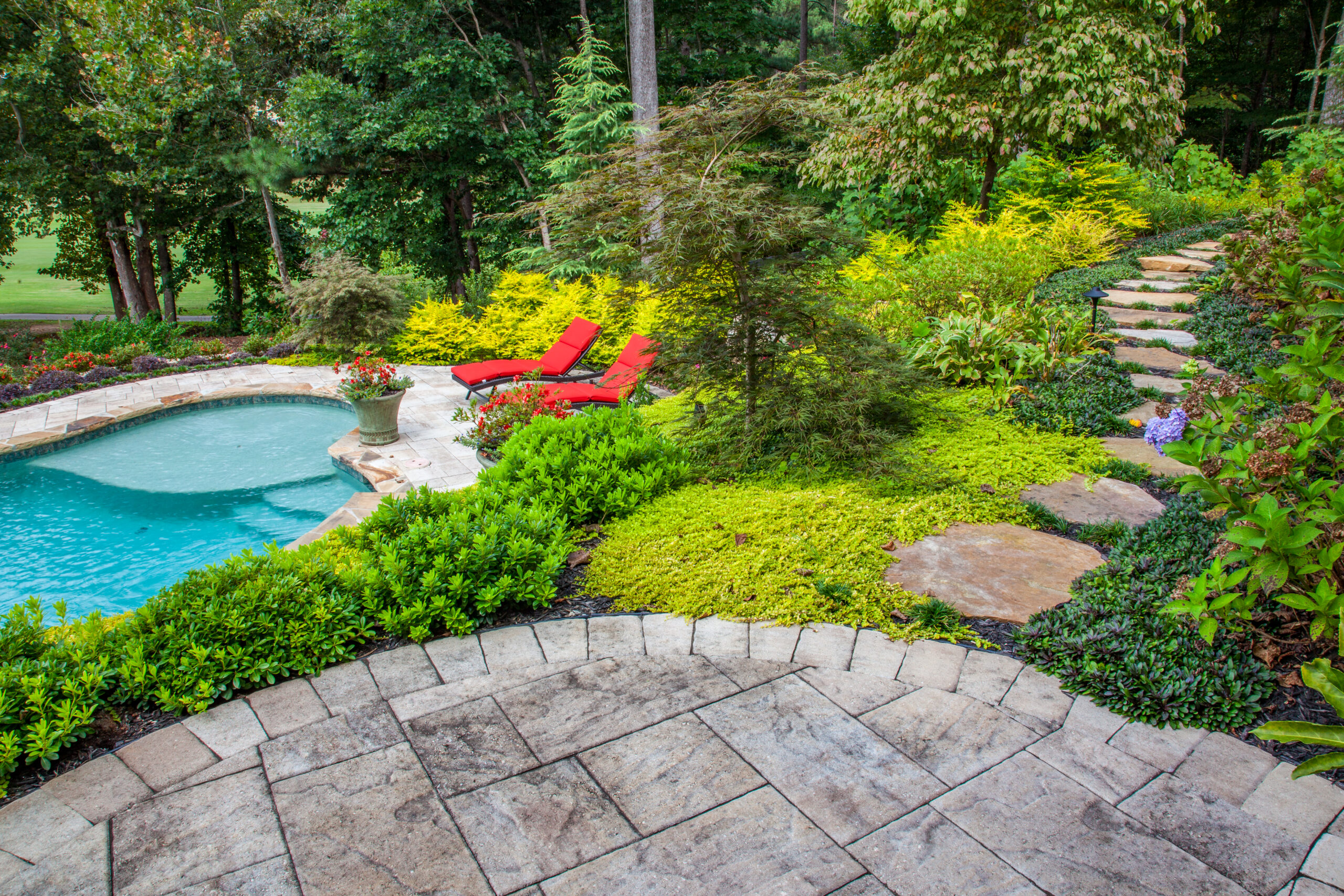 The view from a backyard patio with stepping stones surrounded by ground cover greenery leading to the side yard and a pool