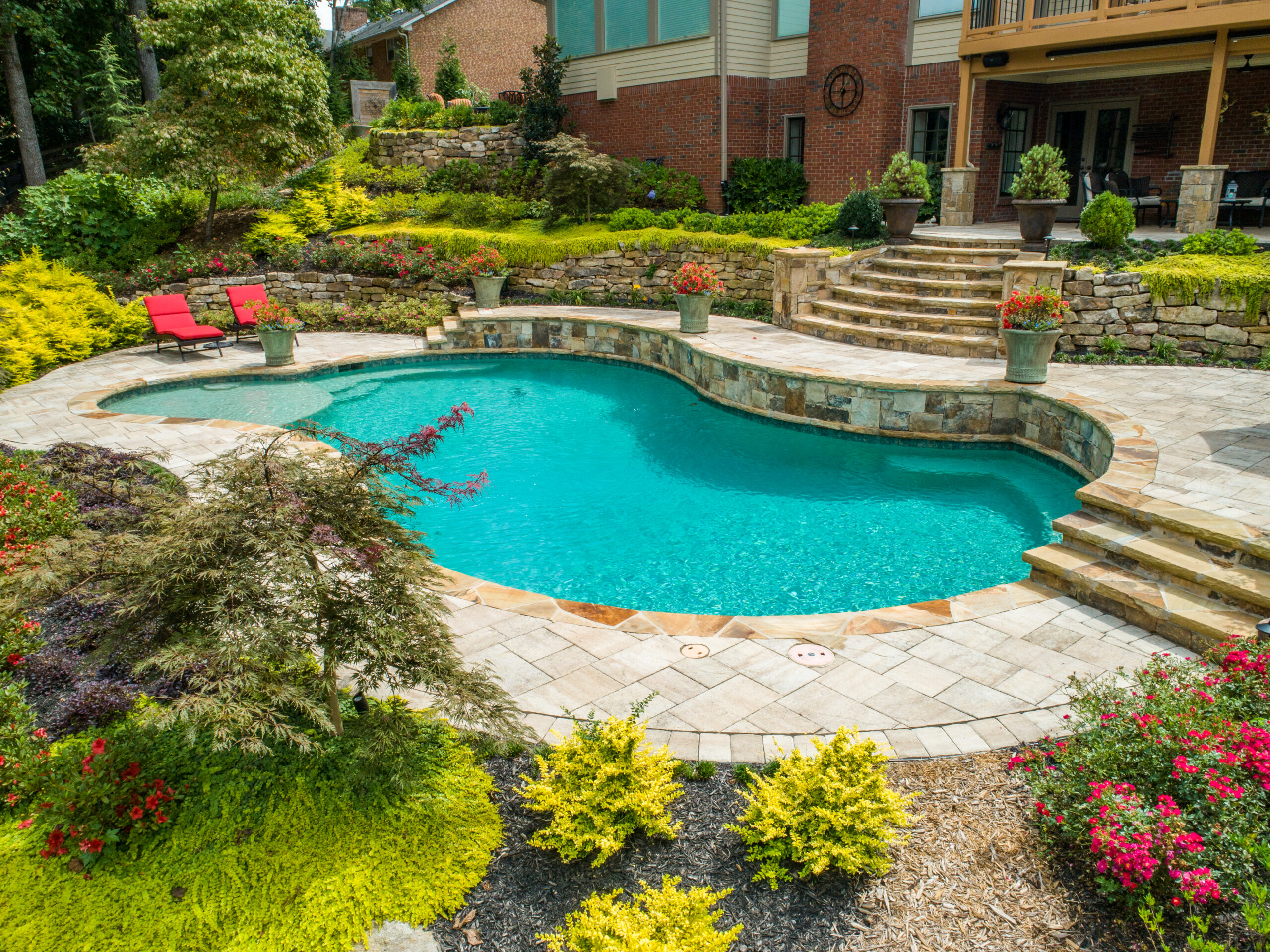 A turquoise pool with flagstone coping and ledgestone retaining walls surrounded by landscaping and greenery