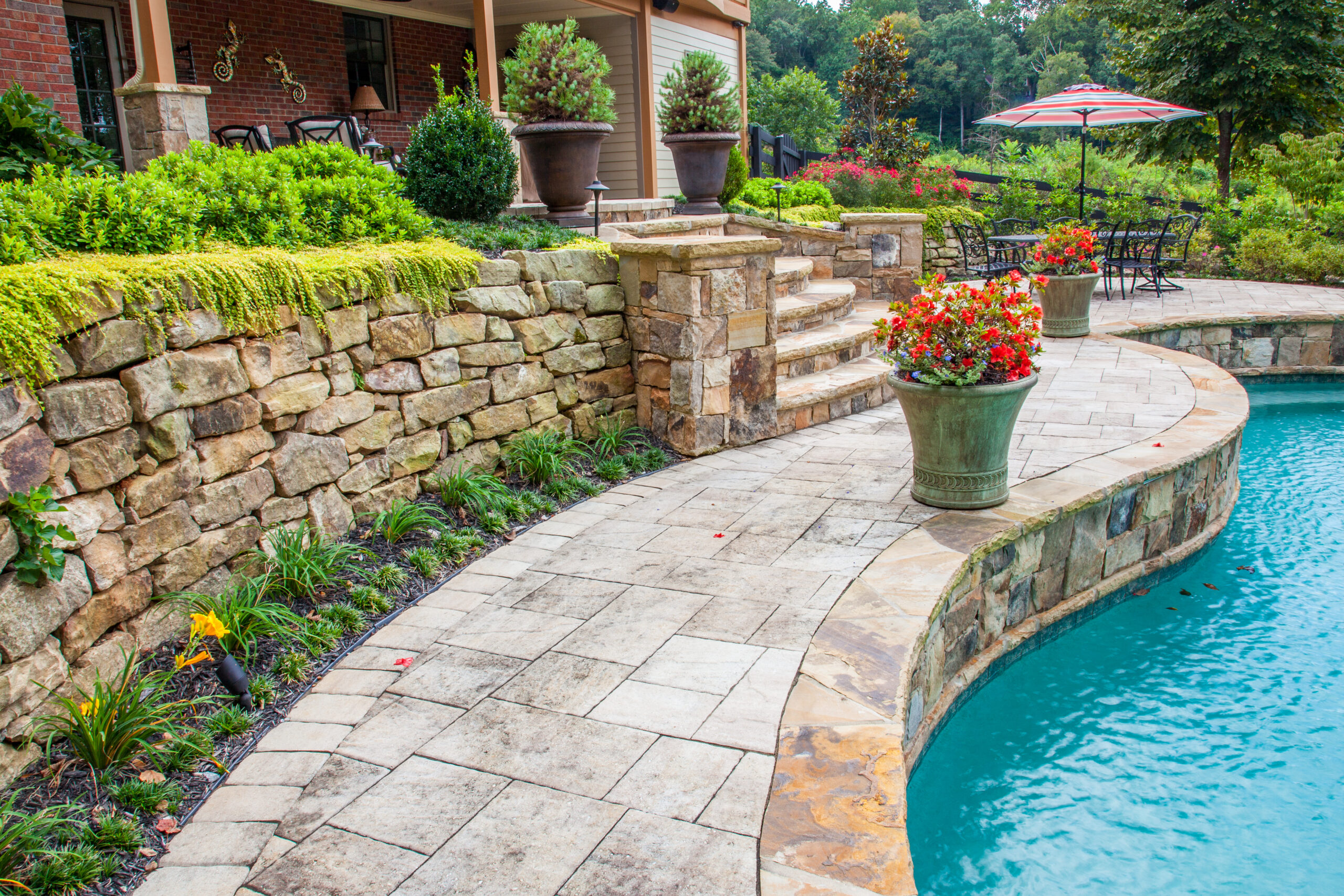 A fieldstone retaining wall with landscaping and greenery over a pool