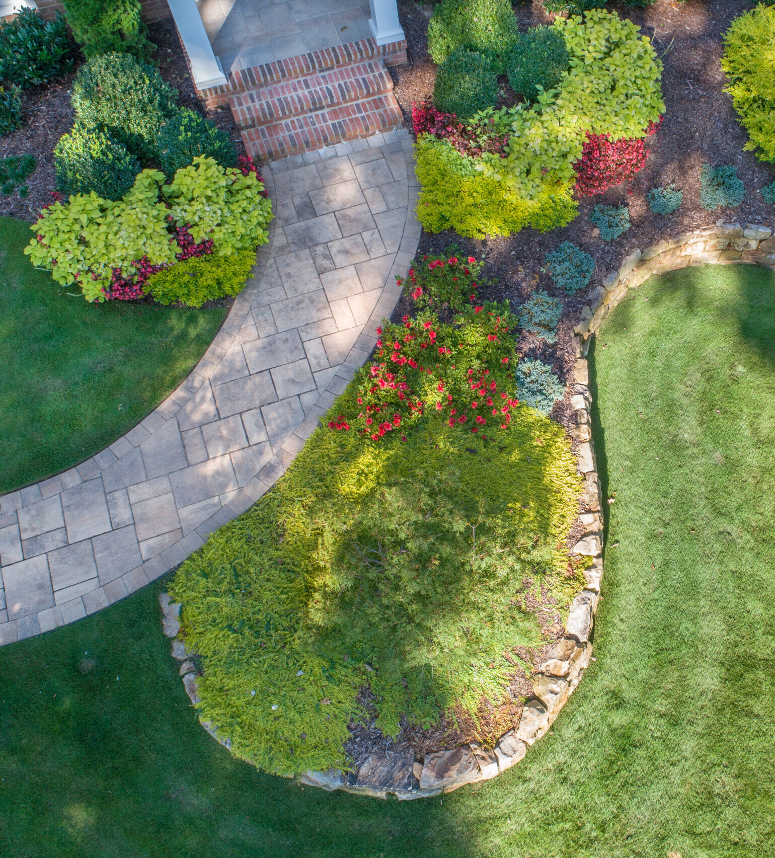 A drone shot of the raised beds in front of a brick house with gorgeous greenery