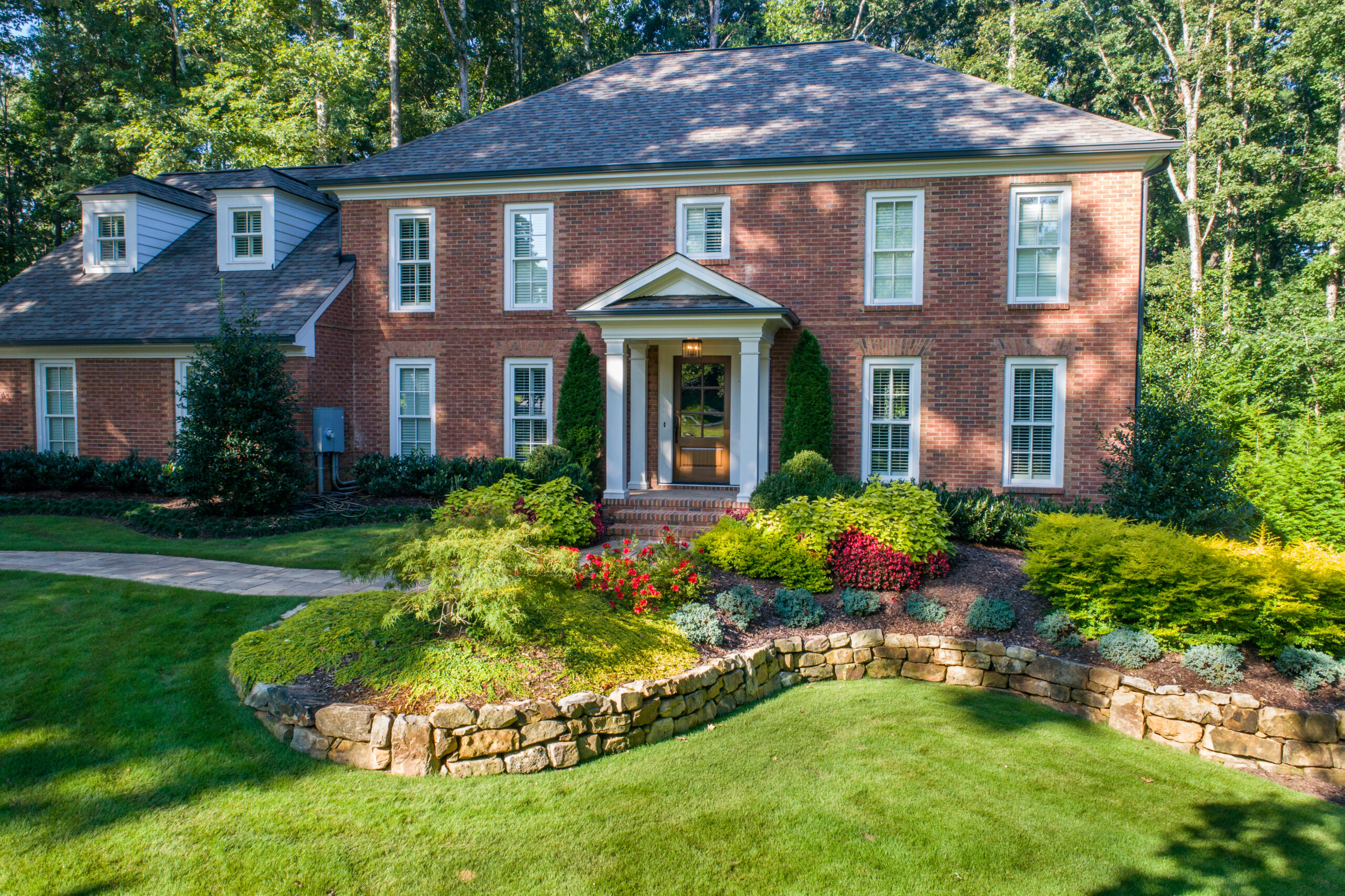 The front of a brick house with a gorgeous garden filled with greenery