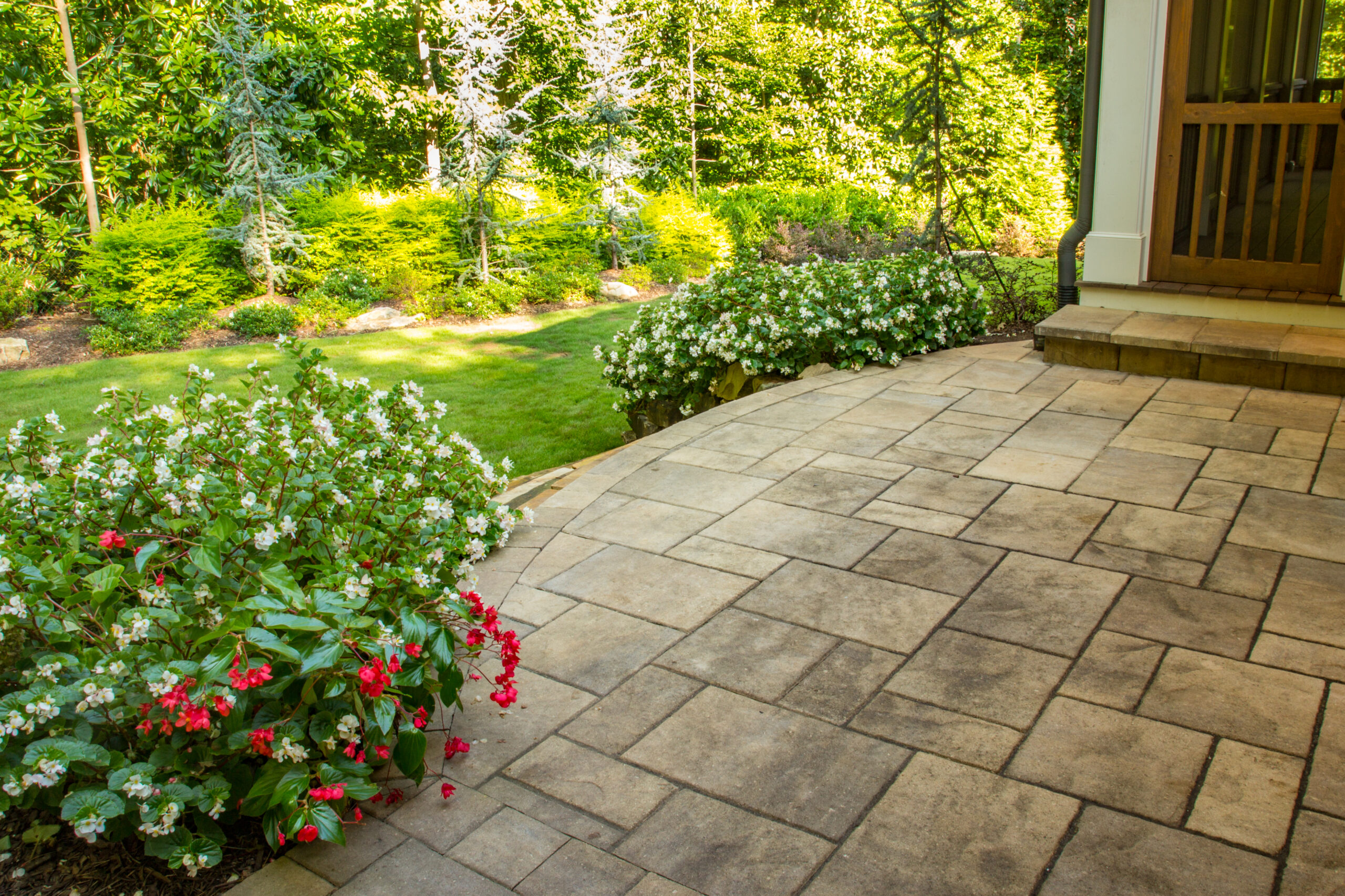 The view of a backyard from a stone patio surrounded by greenery