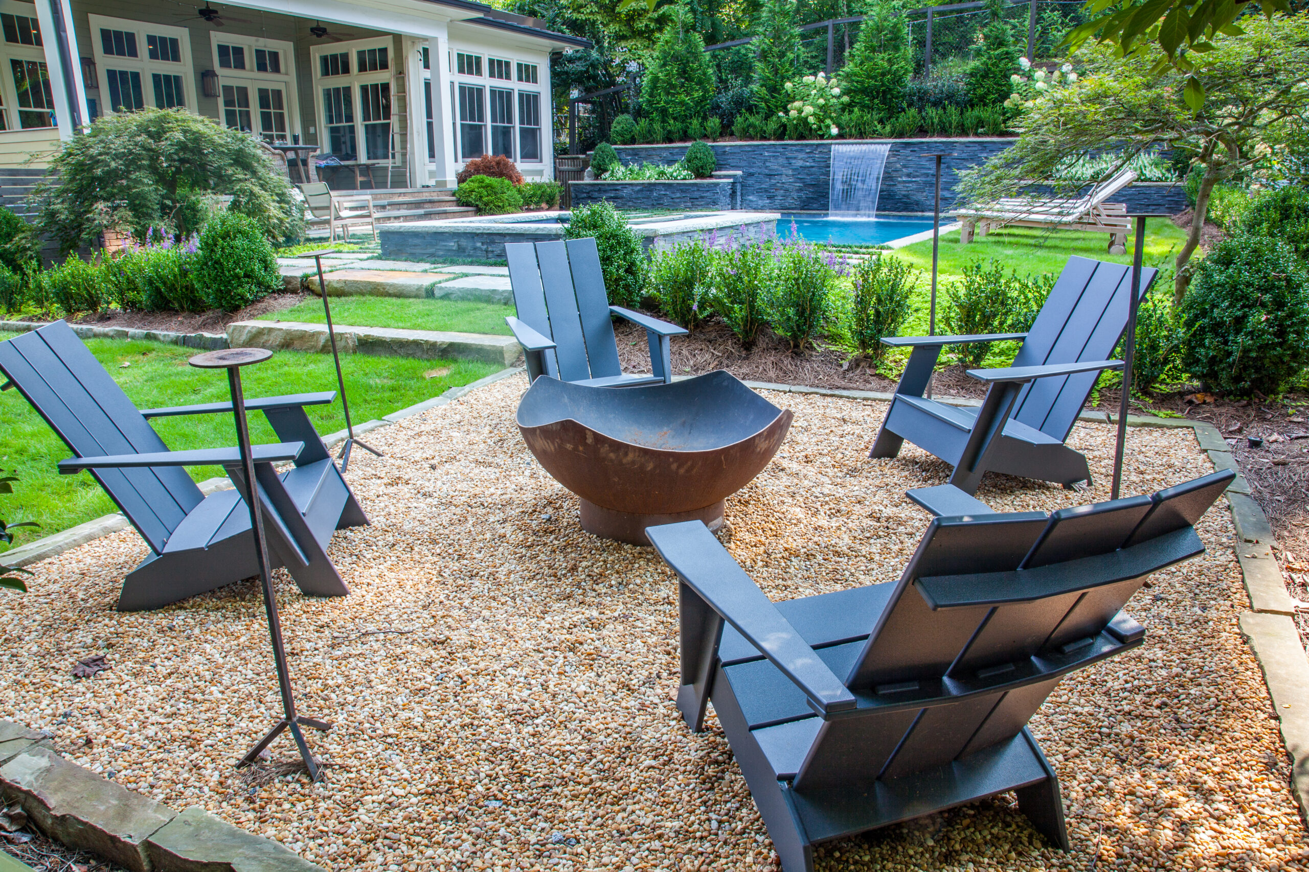 a modern fire pit in a backyard with four Adirondack chairs