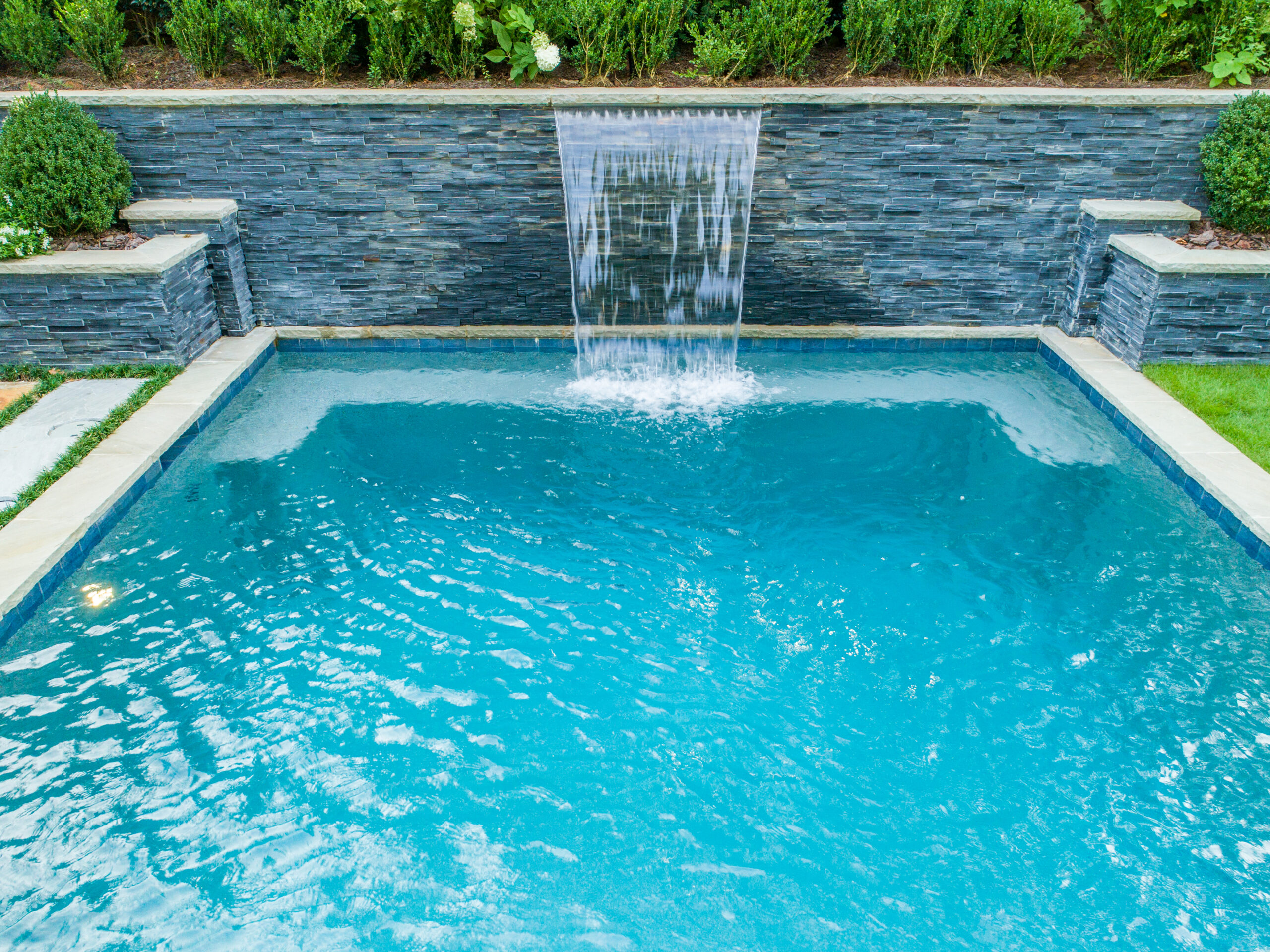 A pool against a ledgestone retaining wall with a spillway waterfall fountain