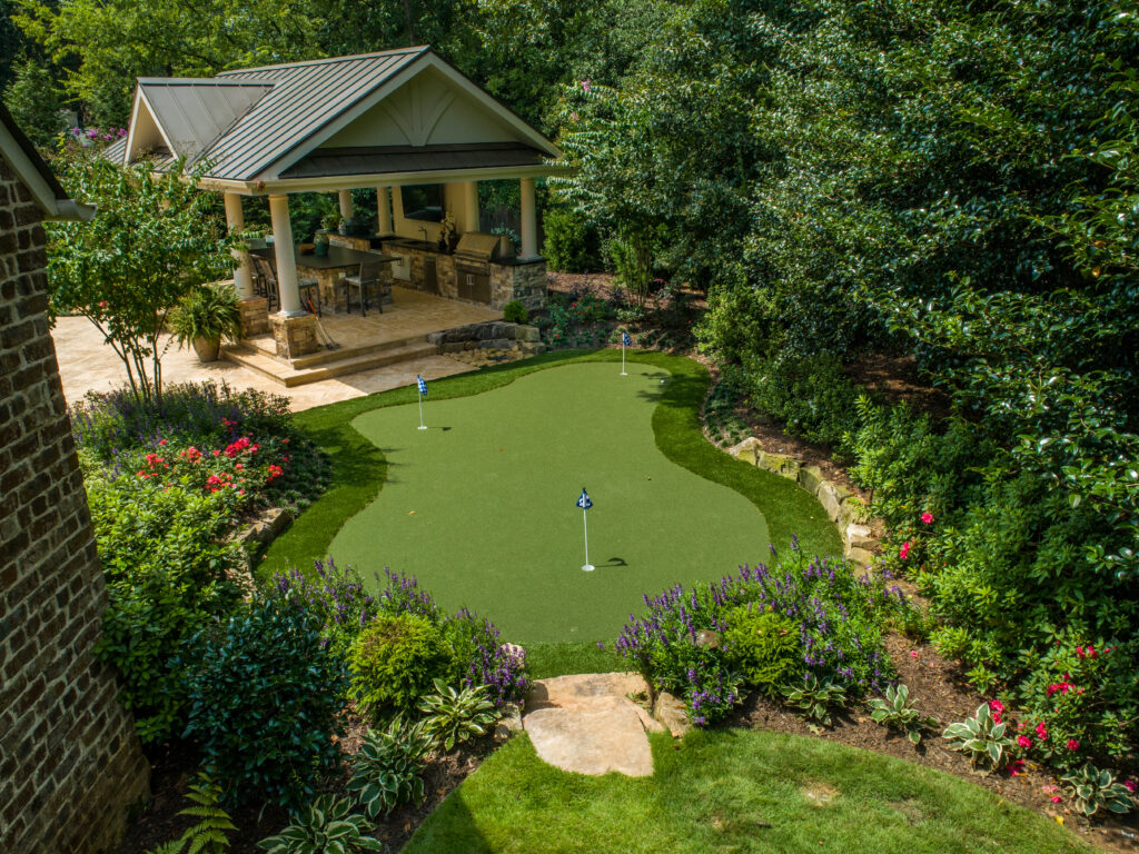 an overhead shot of a putting green with an outdoor kitchen in the background